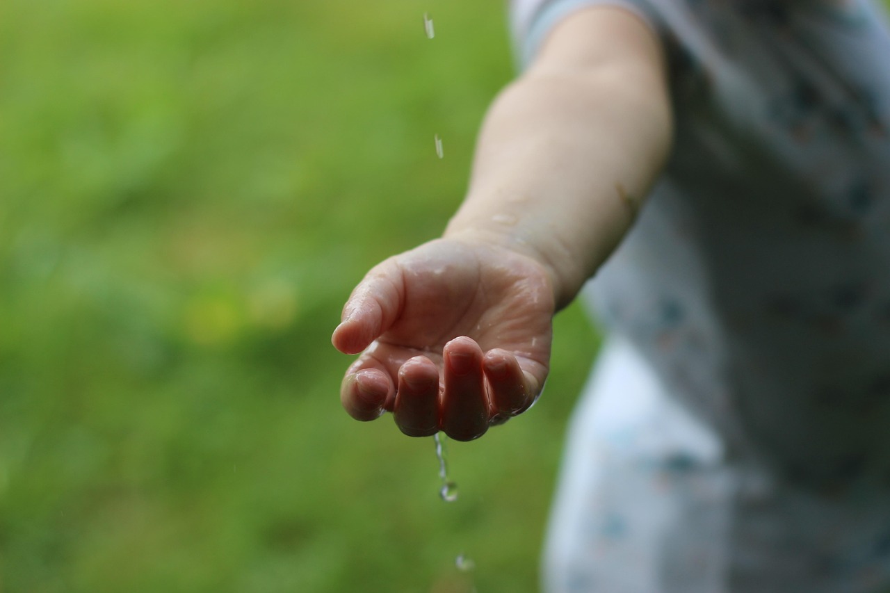 Eine Hand im Grünen, auf die Wasser tröpfelt